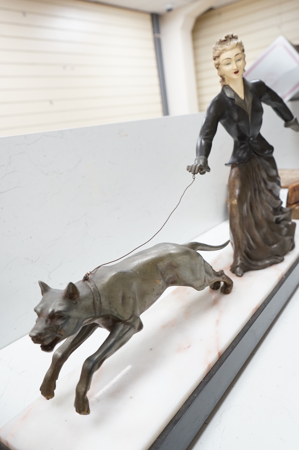 An Art Deco French spelter and ivorine model ‘Walkies Lady and Dog’, on a black marble and cream onyx base, 75cm long